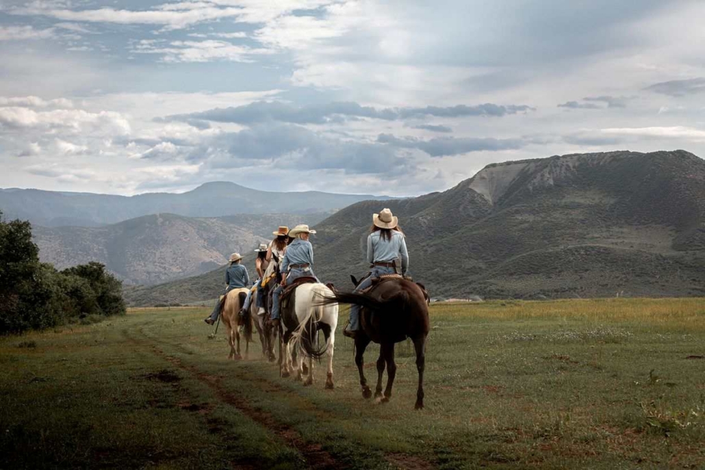 A diverse group of tourist enjoys horseback riding through a picturesque field in Aspen during the colorful October season.