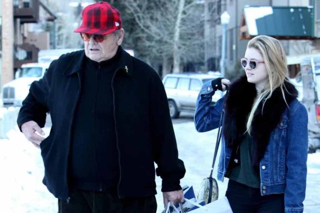 Jack Nicholson walks alongside a young woman on a street in Aspen, surrounded by beautiful mountain scenery.