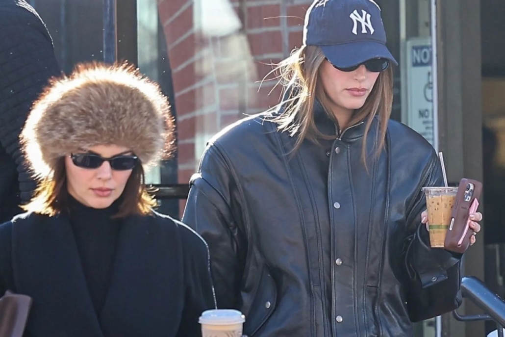 Two women, including Kendall Jenner, in black jackets and hats, walking together down a city street.