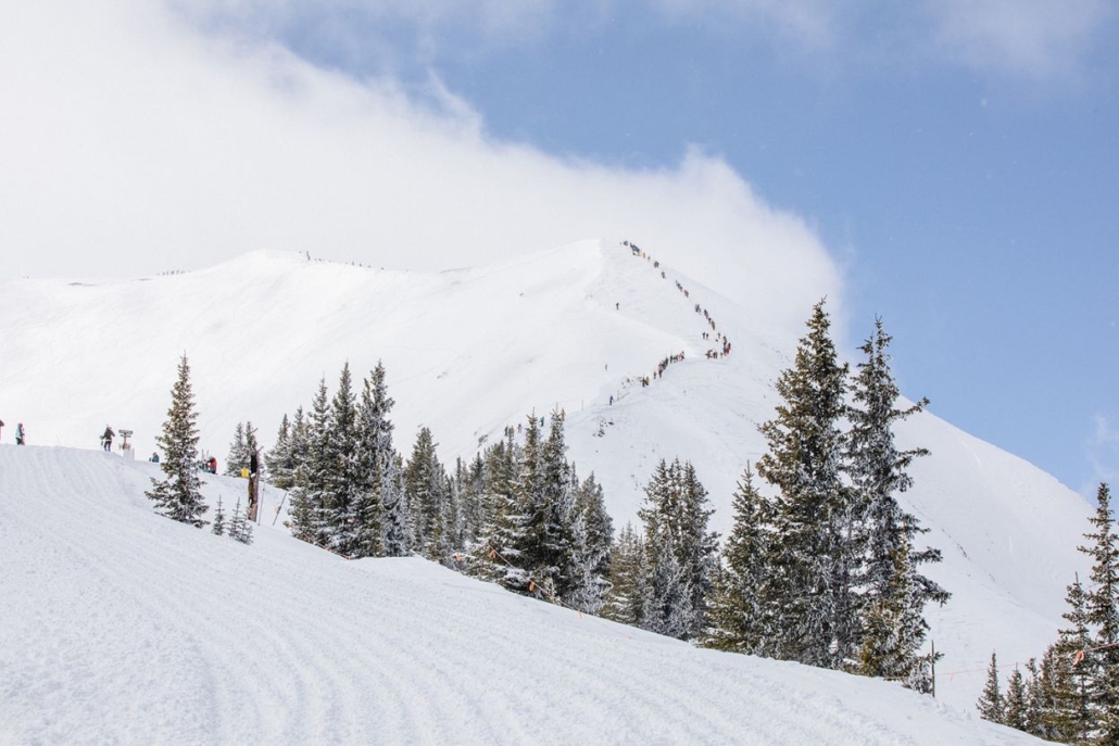 A snowboarder descends a snowy slope at Highland Bowl in Aspen, surrounded by winter scenery.