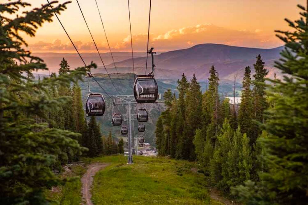 Gondola ascending Aspen Mountain at sunset, with forested slopes and panoramic mountain views in summer.