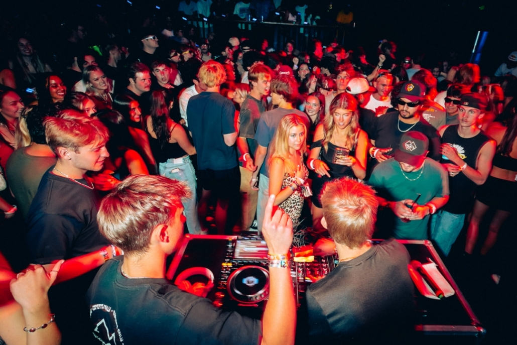 Packed nightclub with DJ and partygoers dancing under red lights, electric nightlife scene for an unforgettable celebration.