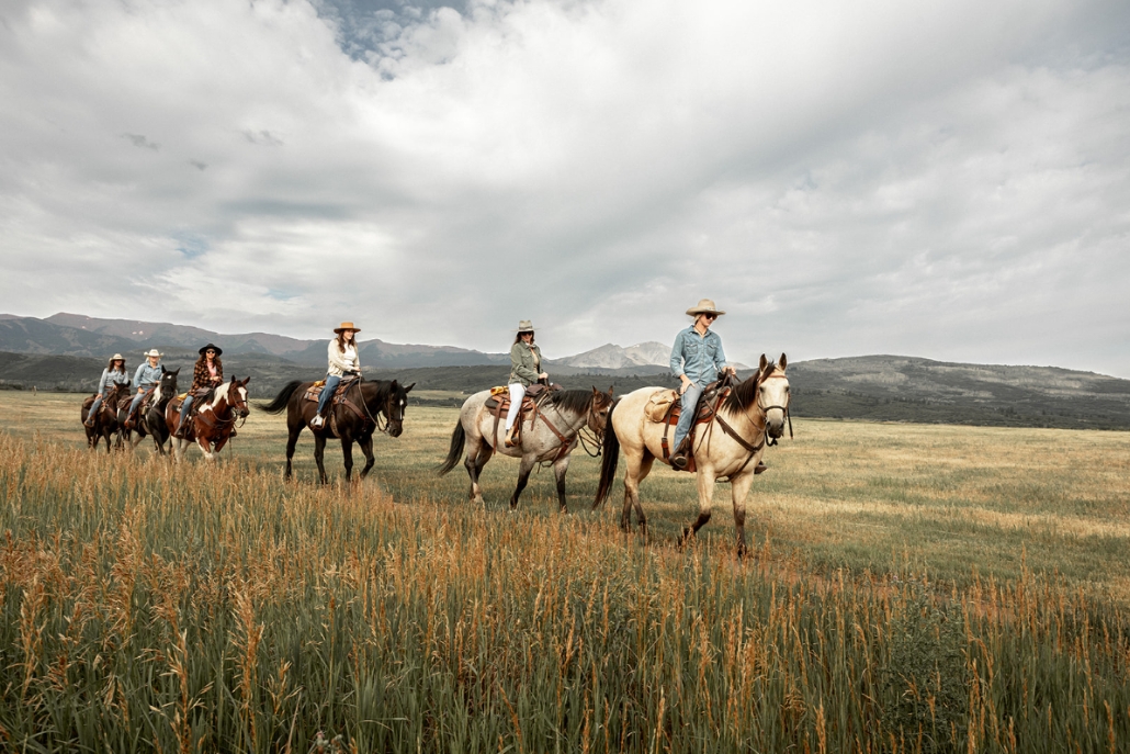 A group of riders on horseback traverses a colorful fall field in Aspen during a private horseback riding experience.