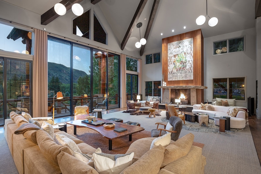 Spacious living room featuring a fireplace and large windows, showcasing the fall scenery at The Riverbend House in Aspen.
