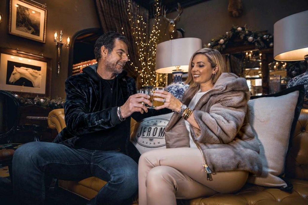 Couple toasting drinks in a cozy, festive lounge at Hotel Jerome during Christmas in Aspen.