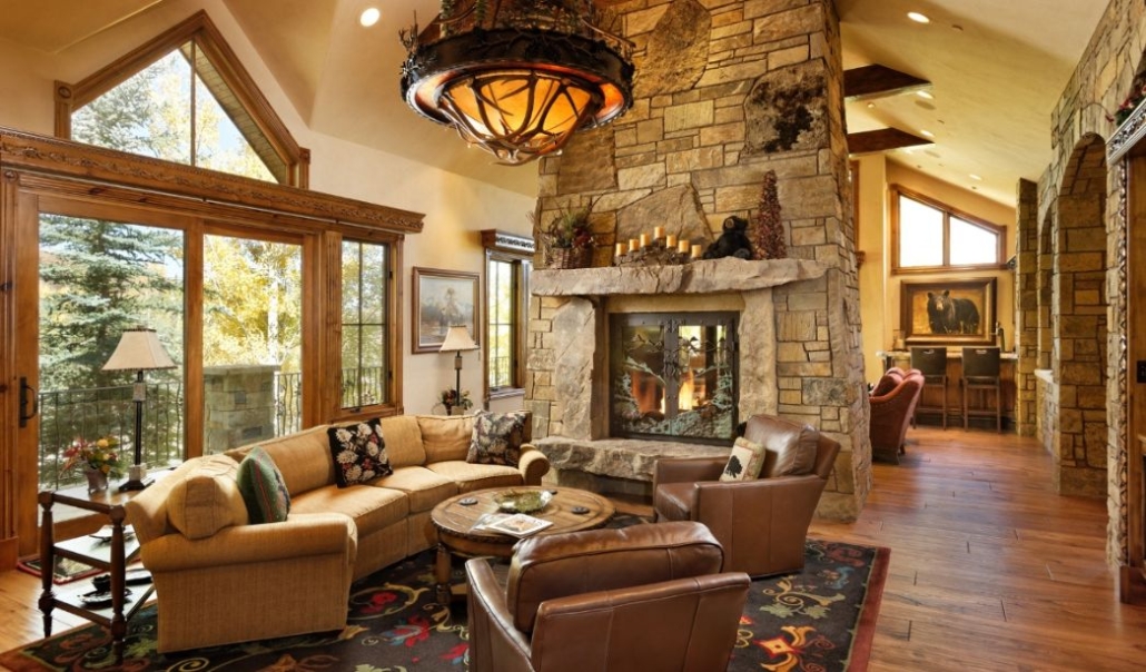 Warm, rustic living room at Serviceberry Summit Estate in Snowmass Village, featuring a stone fireplace, leather chairs, and mountain views through large windows.