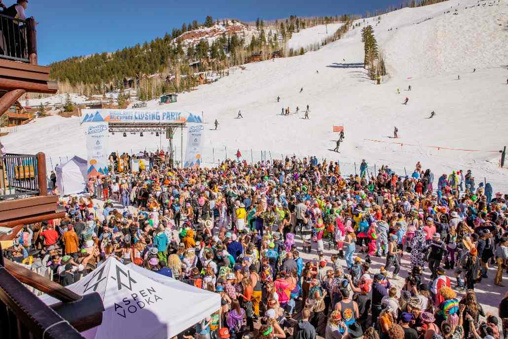 A lively crowd gathers at the top of a ski slope during the Aspen Party Scene closing parties, enjoying the festive atmosphere.