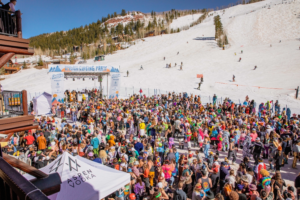 A lively crowd gathers at the top of a ski slope during the Aspen Party Scene closing parties, enjoying the festive atmosphere.