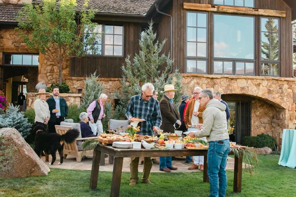 A lively gathering of people around a table filled with food and drinks, creating a festive Aspen party atmosphere.