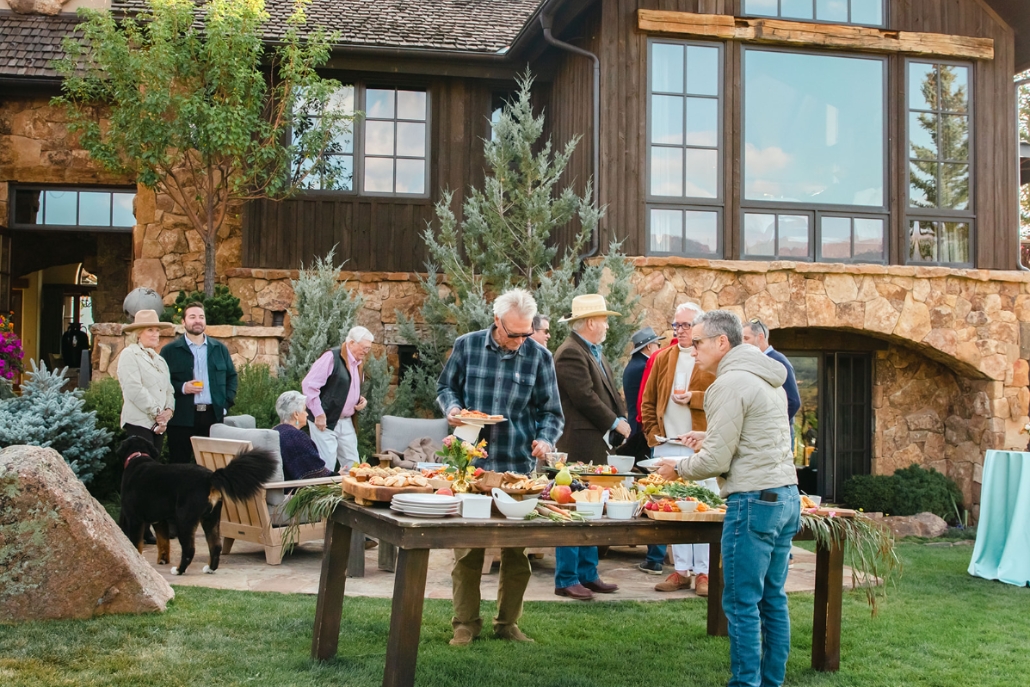 A lively gathering of people around a table filled with food and drinks, creating a festive Aspen party atmosphere.