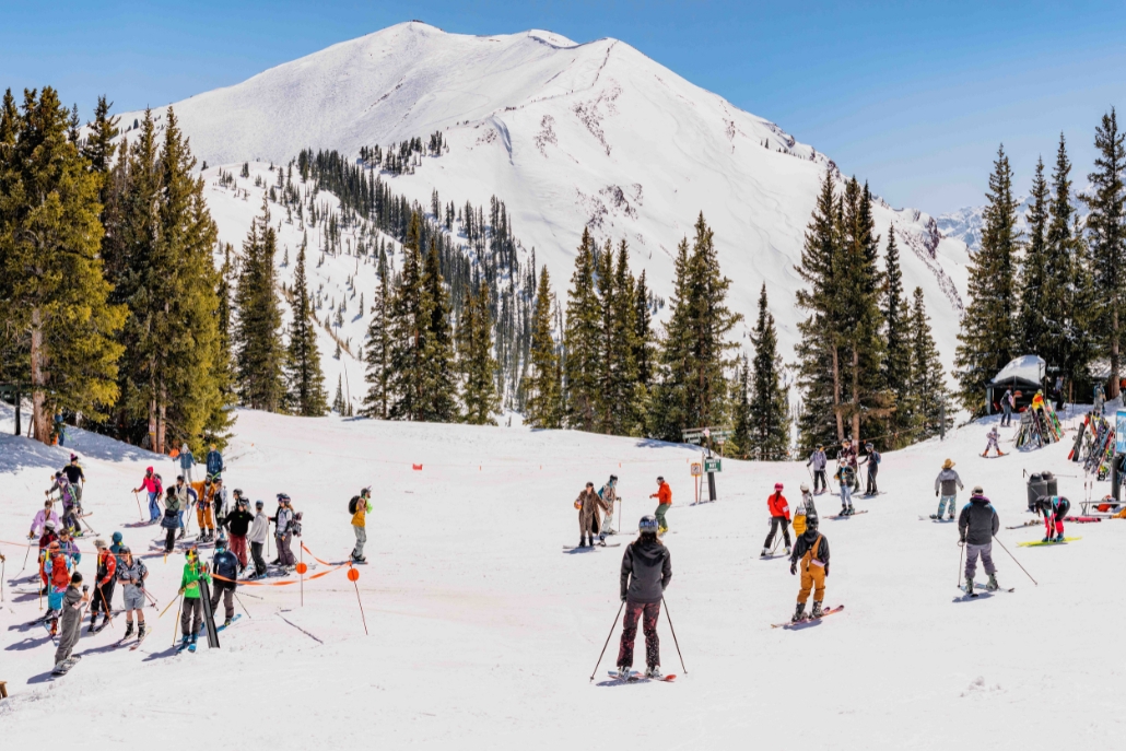 A diverse crowd of people skiing together in the snow, celebrating Aspen Gay Ski Week with joy and enthusiasm.