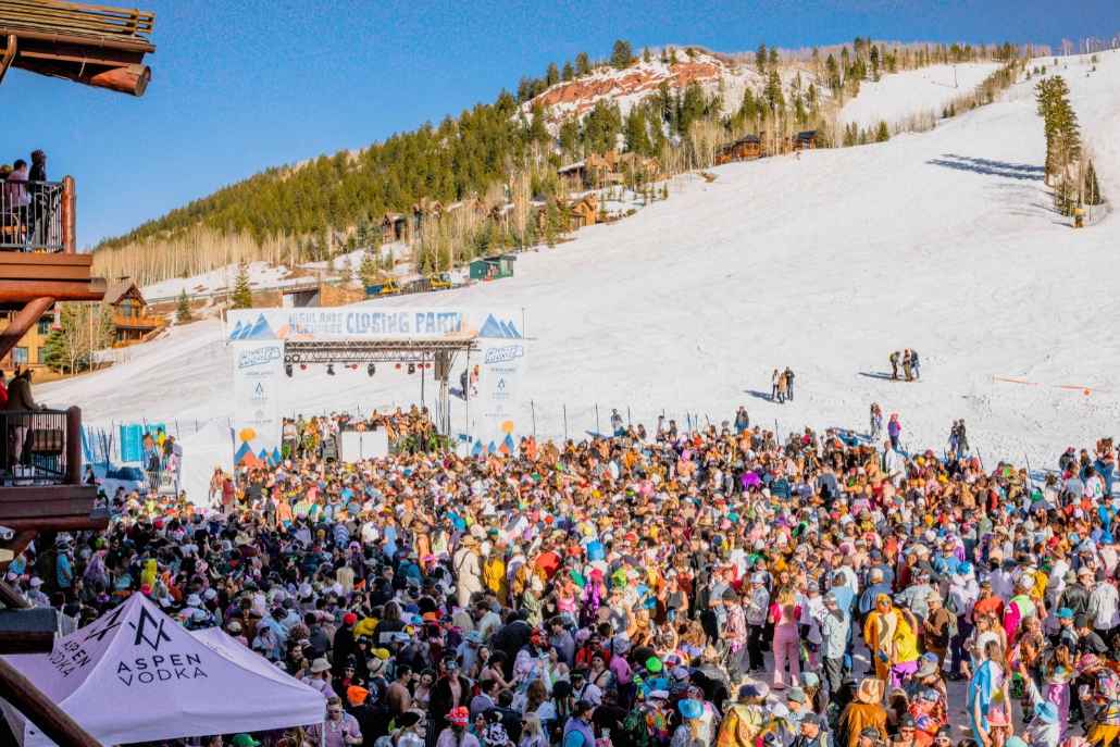 A crowd of people gathers at the top of a ski slope, enjoying the view and atmosphere during an annual event in Aspen.