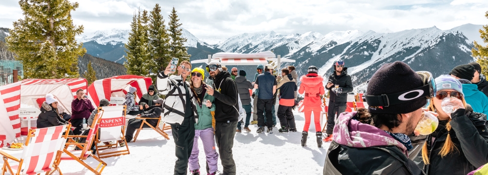 People stand on a snow-covered slope with chairs and umbrellas, enjoying activities in Aspen beyond skiing.