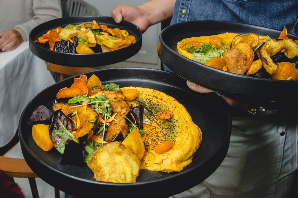 A man presents a plates of colorful vegetable dishes, showcasing local cuisine in Aspen beyond skiing activities.