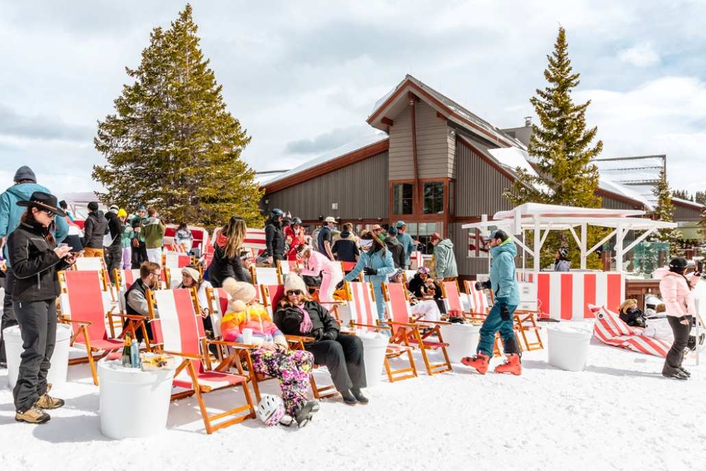 A group of people relaxes in lawn chairs on a snowy hill, enjoying the après experience in Aspen.