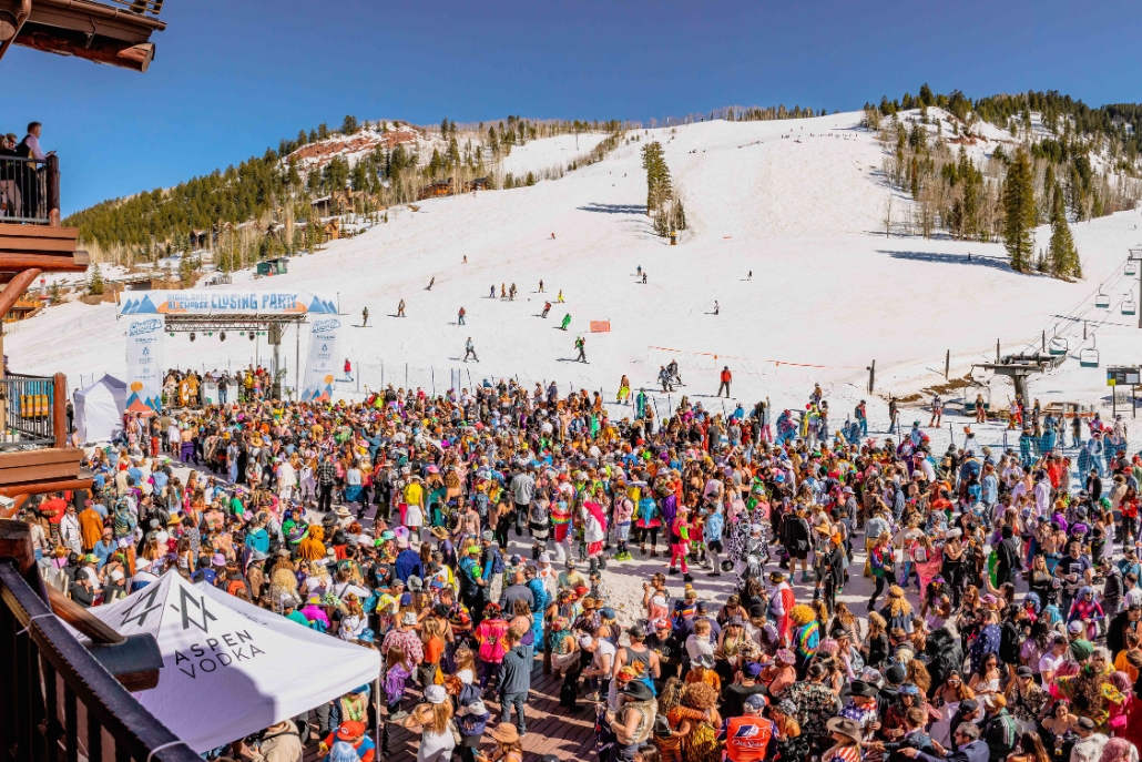 A lively crowd at the peak of a ski slope, partaking in Aspen, Colorado's Spring Break events and parties.