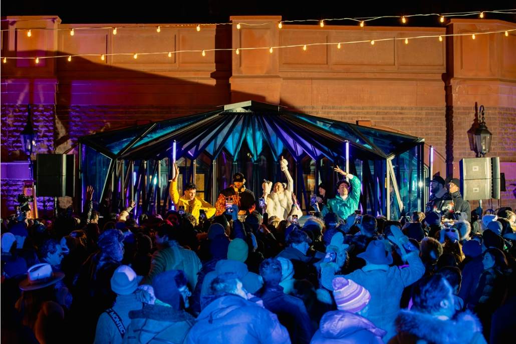 Crowd enjoying a lively après-ski party at The Snow Lodge in Aspen, featuring colorful lights, DJ performance, and guests in winter attire.