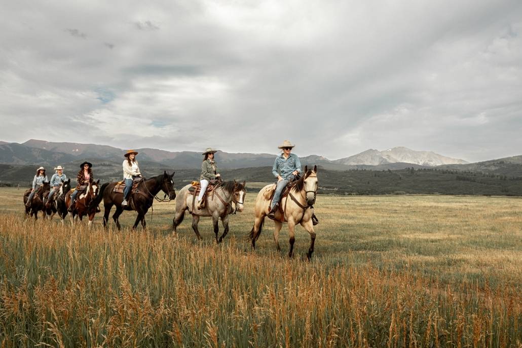 A group of people riding horses through a grassy field, showcasing adventure in Aspen's scenic landscape.