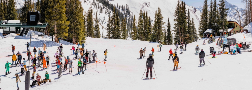 A large group of skiers and snowboarders enjoying the slopes in Aspen during March, surrounded by snow-covered mountains.