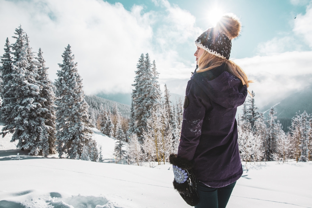 A woman in a purple coat stands on a snowy mountain, showcasing winter fashion in Aspen during March.