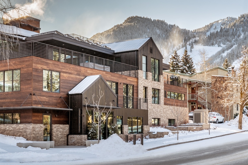 A modern building set against a snowy mountain backdrop in Aspen, showcasing winter accommodations in March.