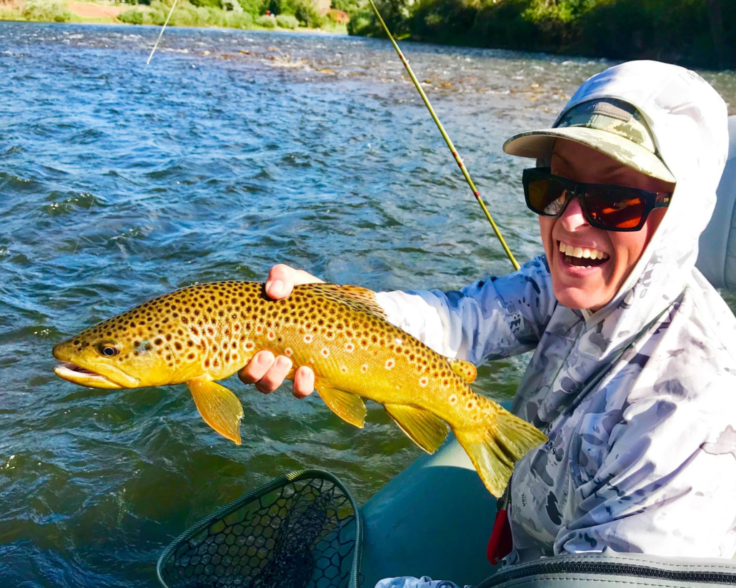 Person fly fishing in Aspen Colorado holding a freshly caught trout in a mountain river