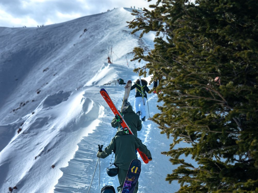 Skiers hiking along a snowy ridge at Highland Bowl in Aspen Colorado with mountain views