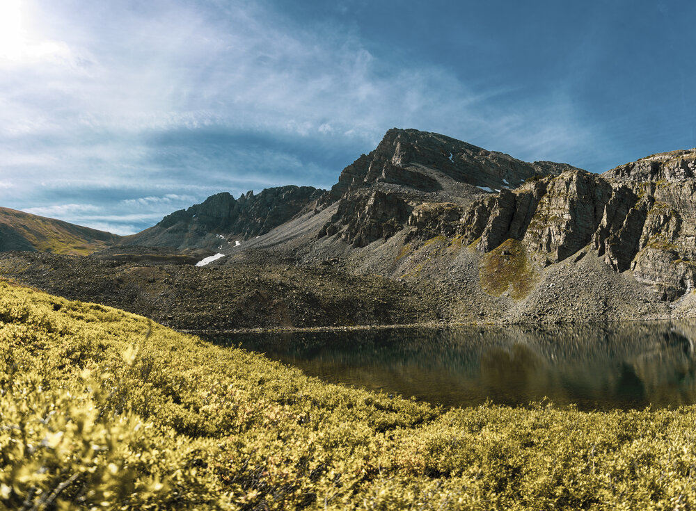 Scenic mountain lake and rugged hiking trail in Aspen Colorado surrounded by rocky peaks and blue sky