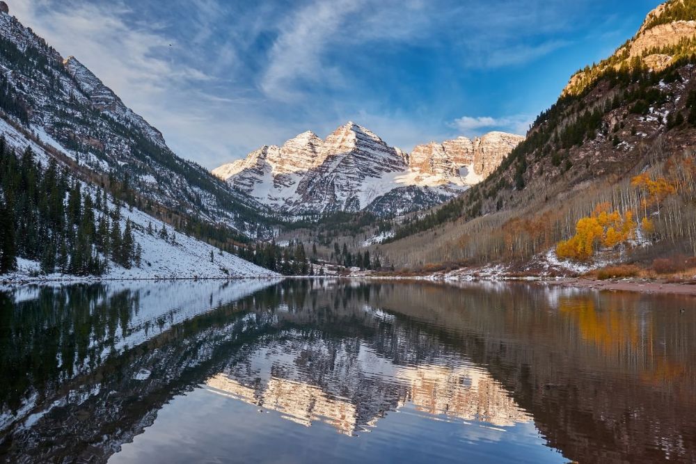Maroon Bells mountains reflected in a lake during fall and winter in Aspen Colorado