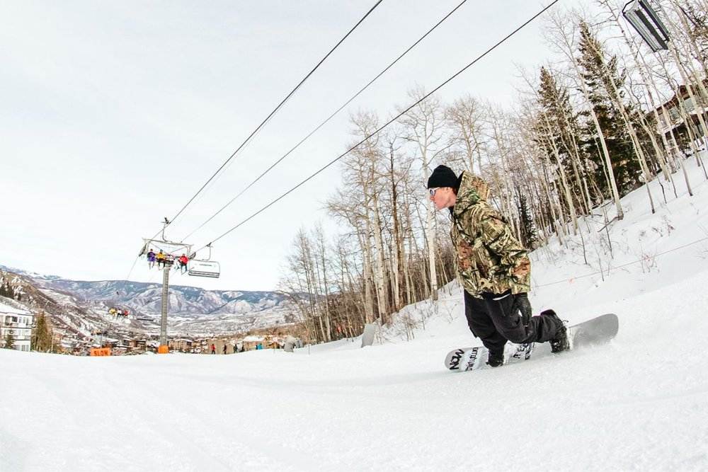 Snowboarder riding down a slope in Aspen Colorado with mountain views and ski lift in the background