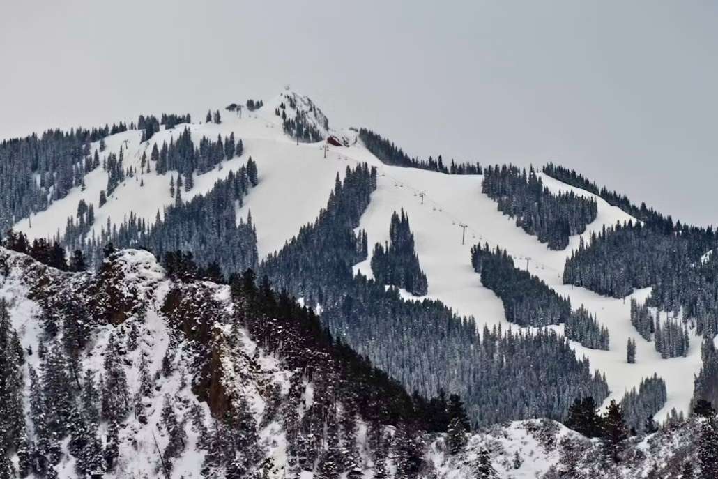 Snow-covered ski slopes at Aspen Highlands surrounded by dense evergreen forest