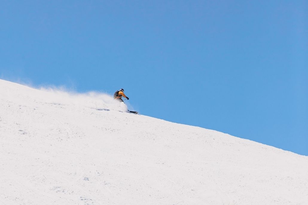 Skier carving fresh powder on Aspen Mountain beneath a clear blue winter sky