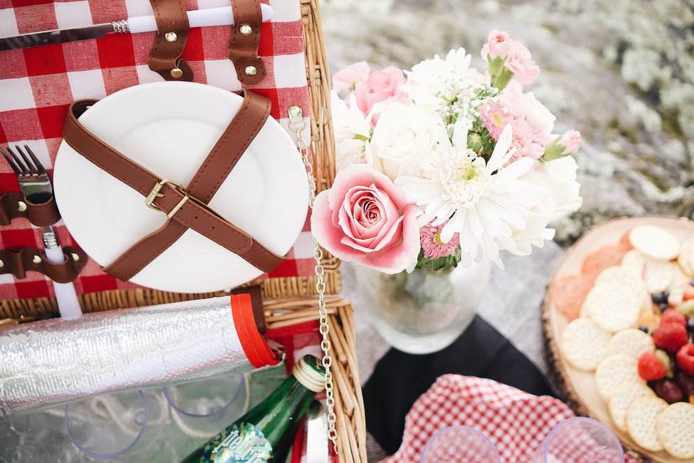Spring picnic setup with a wicker basket, fresh flowers, plates, and snacks for an outdoor day in Aspen.