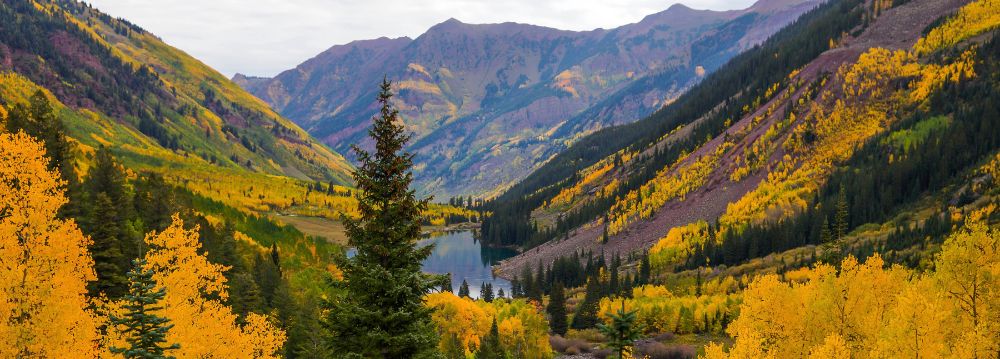 Autumn view of Maroon Bells in Aspen, Colorado, with golden aspen trees, mountain peaks, and a lake.