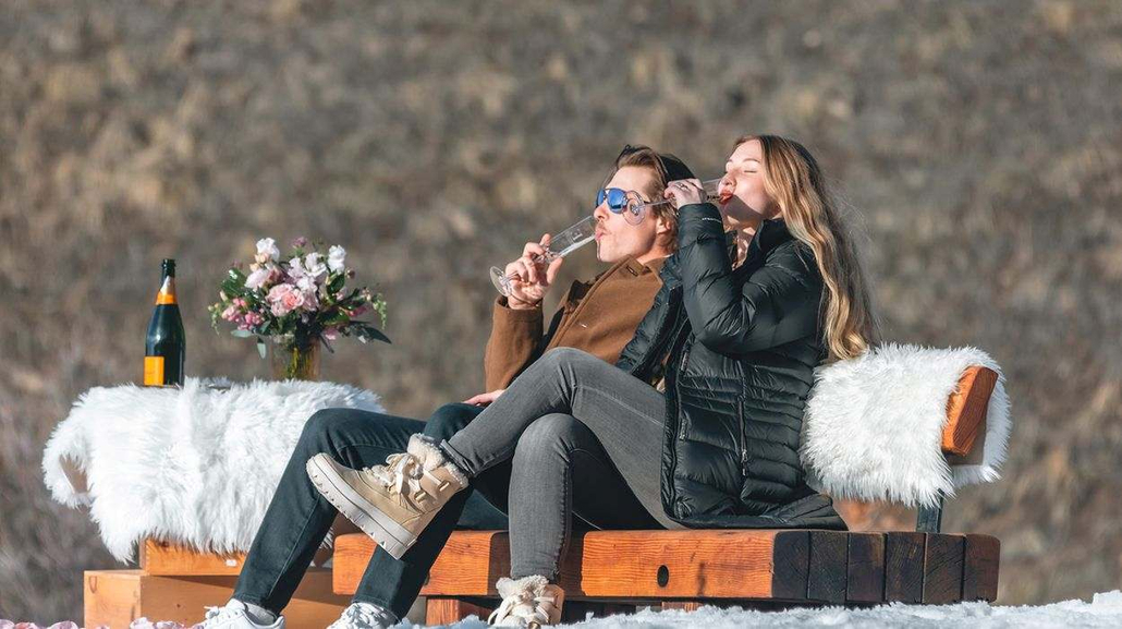 Couple wearing winter jackets and boots enjoying champagne outdoors on a snowy day in Aspen, Colorado.