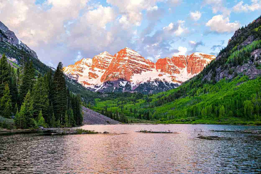 Snow-capped Maroon Bells mountains overlooking a lake and lush green forests near Aspen, Colorado.