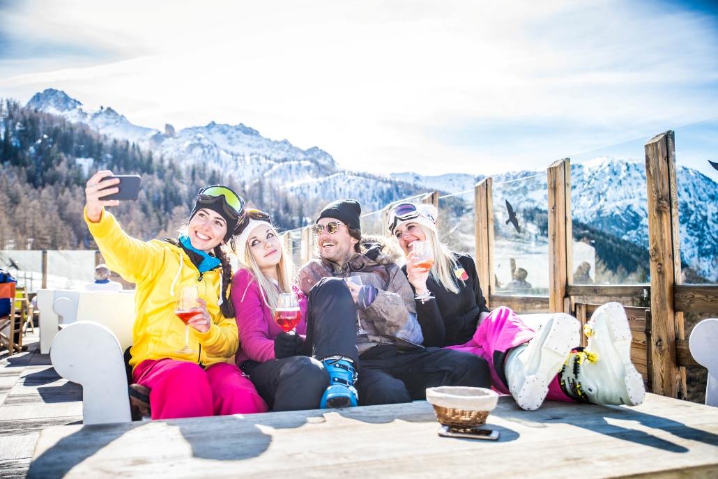 Group of four friends in ski gear taking a selfie and enjoying drinks at a snowy mountain resort in Aspen.